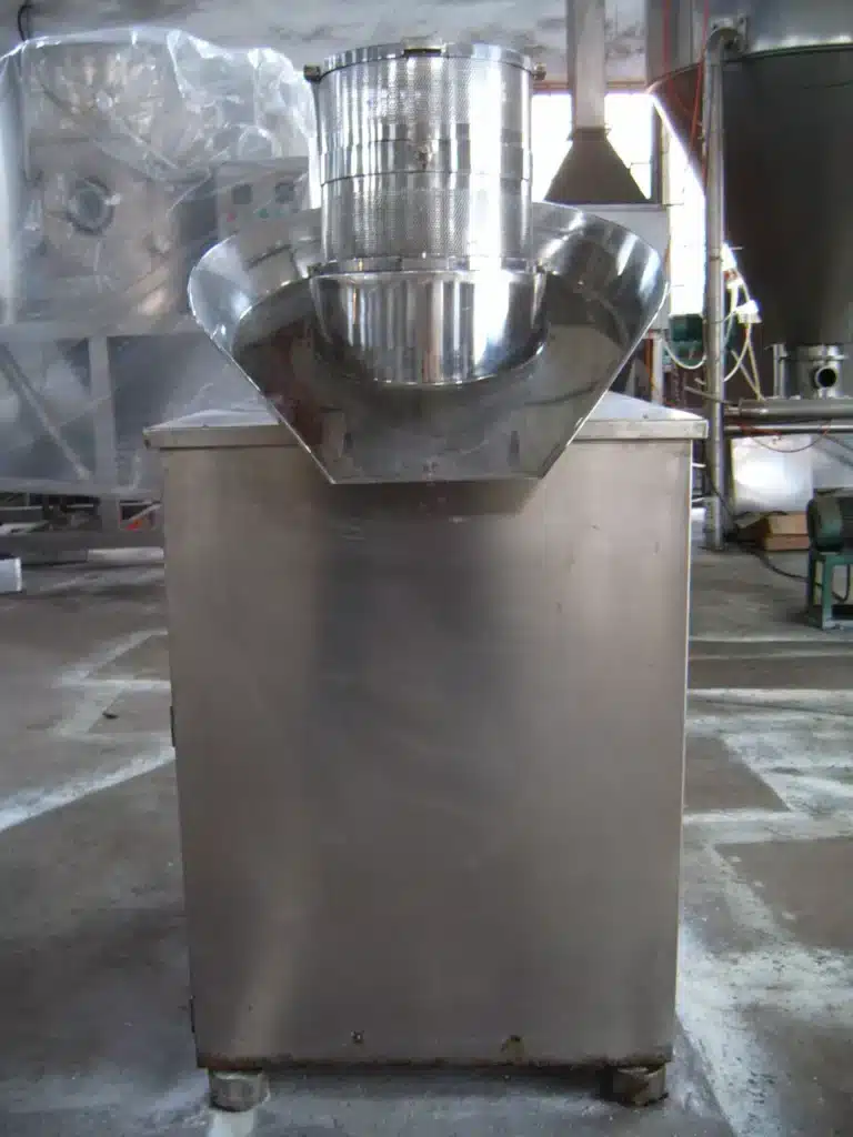 A stainless steel Basket Granulator featuring a mesh drum within a funnel-shaped holder, situated in an industrial workspace.