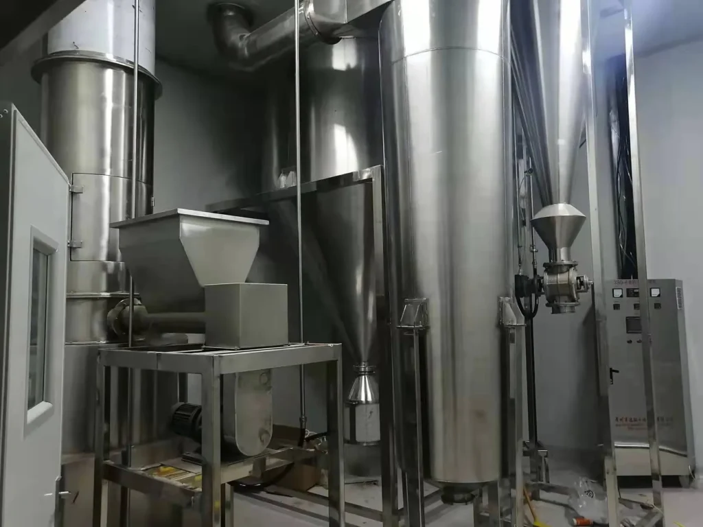 Exterior of an industrial facility displaying two large Spin Flash Dryers with blue cylindrical bodies and conical bases. Connected by a series of metal ducts, they are part of a system likely used for rapid drying of particulate materials, under a partially constructed roof.