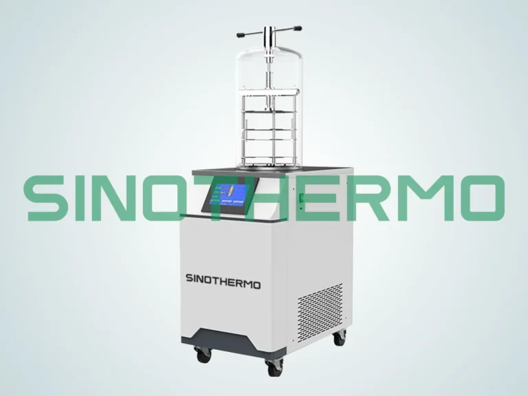 A benchtop freeze dryer with a digital control panel, clear drying chamber, and mounted on wheels, displayed against a plain background.