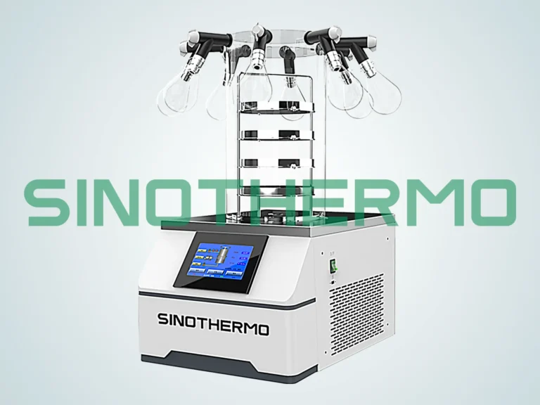 A benchtop freeze dryer from SINOTHERMO with a digital control panel is displayed. The device has a stack of clear chambers connected to a manifold with valves on top, set against a clean, isolated background.