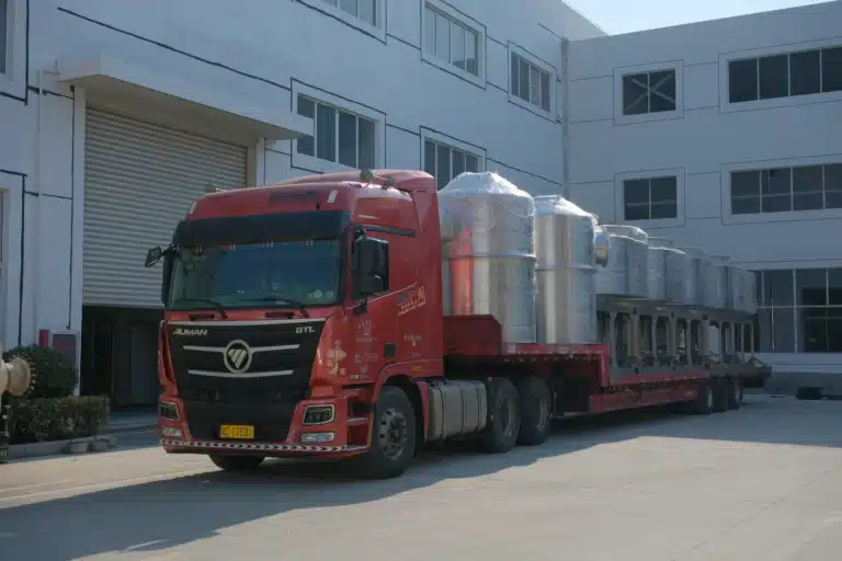 A red transport truck loaded with multiple XSG-14 spin flash dryers wrapped in protective material, ready for delivery outside an industrial facility.
