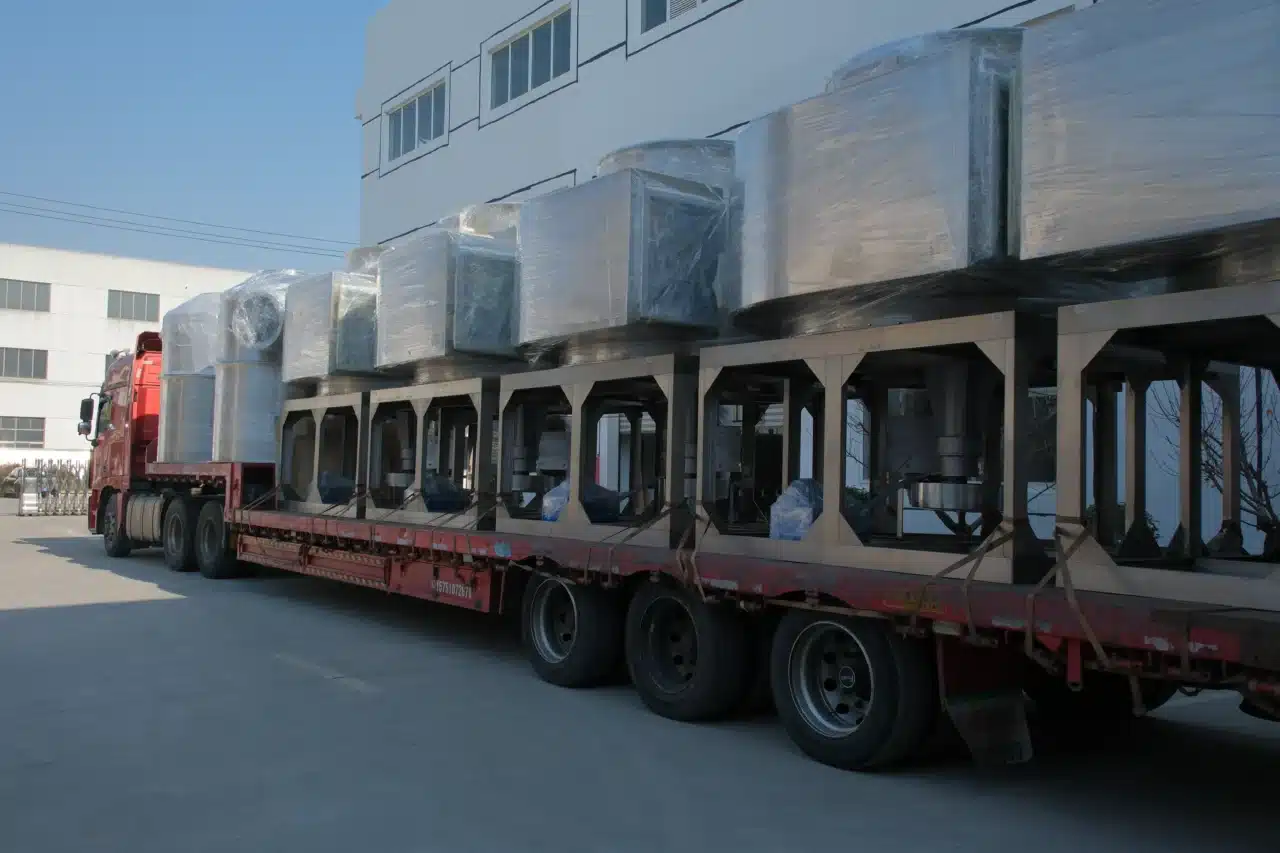 Một chiếc xe tải sàn phẳng màu đỏ chở nhiều máy sấy quay XSG-14 được bọc chắc chắn bằng màng bảo vệ, đỗ bên ngoài một tòa nhà công nghiệp dưới bầu trời quang đãng.